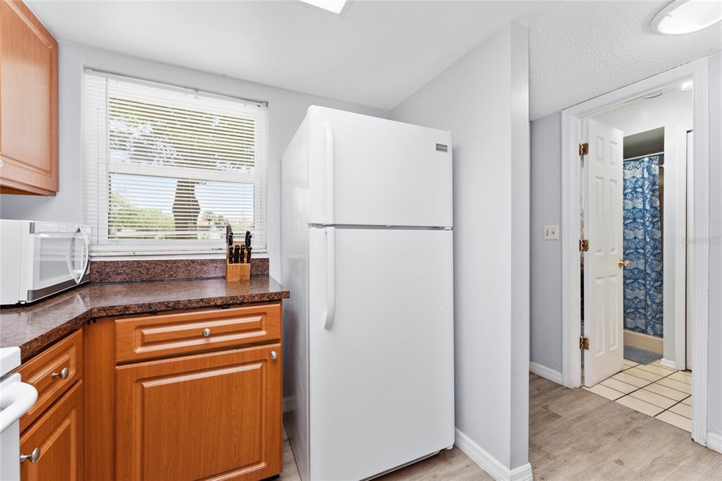 A kitchen features wood cabinets, dark countertops, a white refrigerator, and a doorway to a bathroom — 3118 MAGIC KINGDOM COURT, KISSIMMEE, FL
