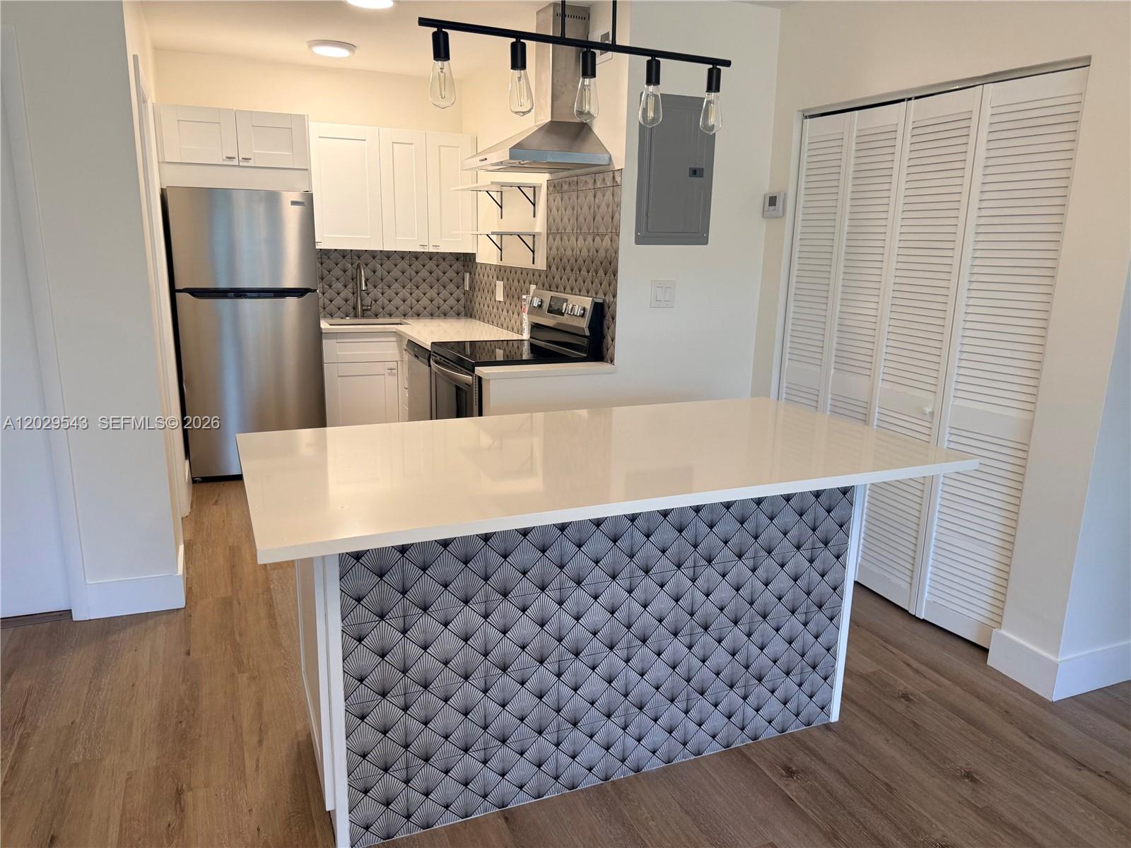 A kitchen features white cabinets, stainless steel appliances, a patterned backsplash, and a breakfast island — 260 S Cypress Rd # 108, Pompano Beach FL 33060, POMPANO BEACH, FL