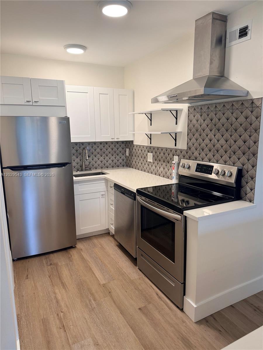 A kitchen features white cabinets, stainless steel appliances, a patterned backsplash, and wood-look flooring — 260 S Cypress Rd # 108, Pompano Beach FL 33060, POMPANO BEACH, FL