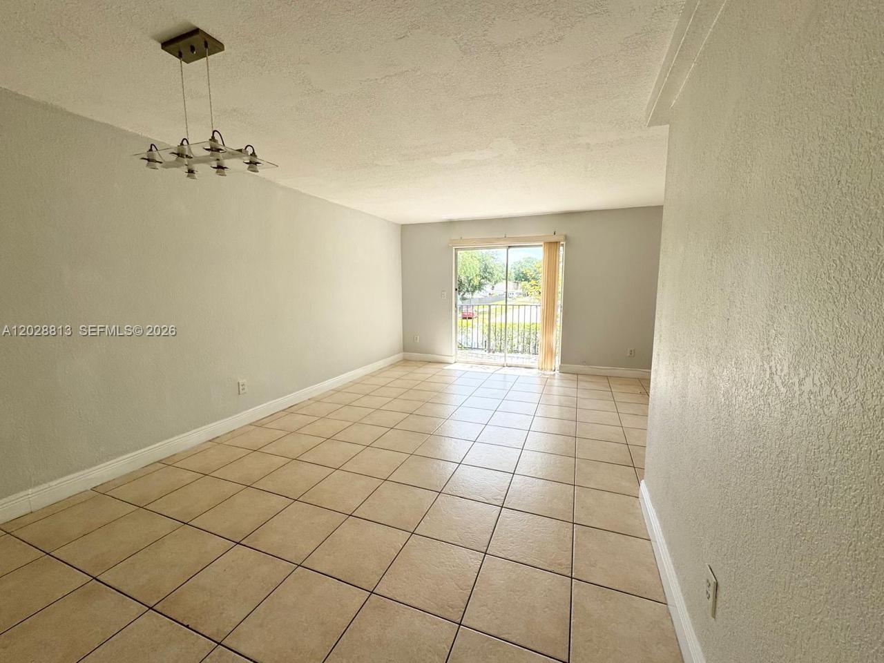 An empty room features light-colored tile flooring, gray walls, a modern chandelier, and sliding glass doors — 8600 SW 109th Ave # 202, Miami FL 33173, MIAMI, FL