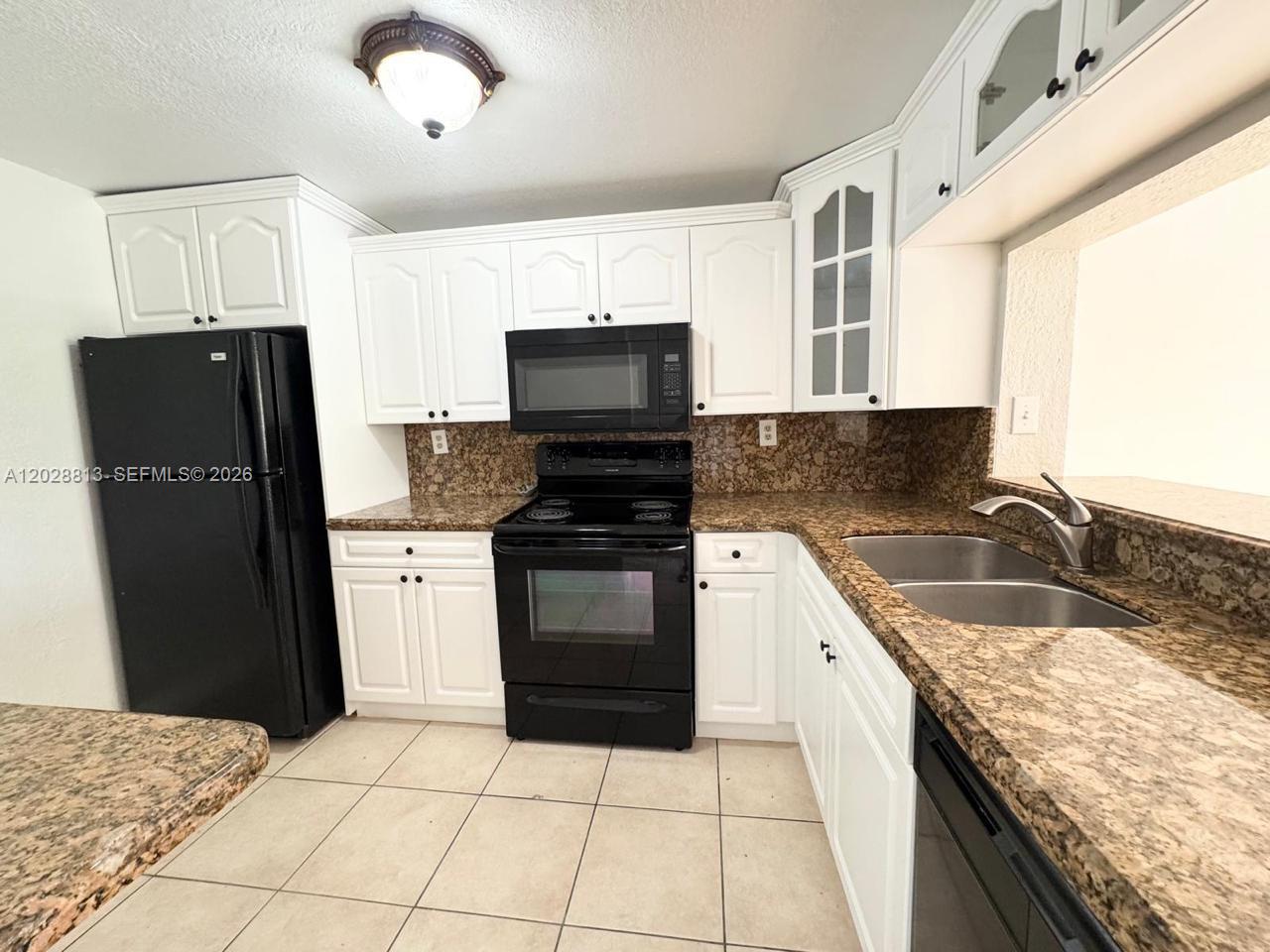 A kitchen features white cabinets, black appliances, and brown granite countertops with tile flooring — 8600 SW 109th Ave # 202, Miami FL 33173, MIAMI, FL