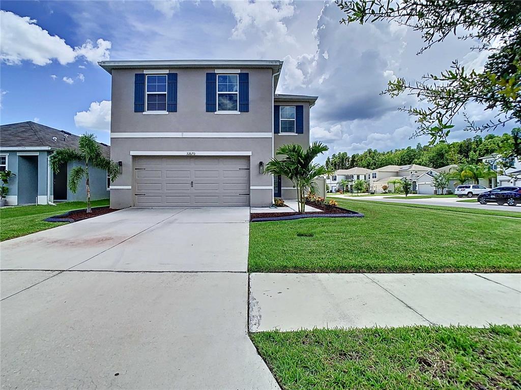 A two-story suburban house with a beige exterior, blue shutters, and a two-car garage — 32670 ANSLEY BLOOM LANE, WESLEY CHAPEL, FL