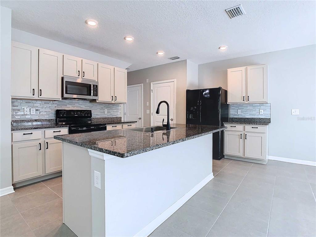 A kitchen features light-colored cabinets, granite countertops, a center island, and black appliances — 32670 ANSLEY BLOOM LANE, WESLEY CHAPEL, FL