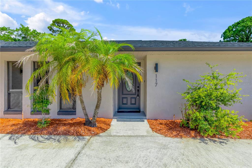 A single-story house exterior features a gray front door, a palm tree, and landscaping — 117 POINCIANA ROAD, EDGEWATER, FL
