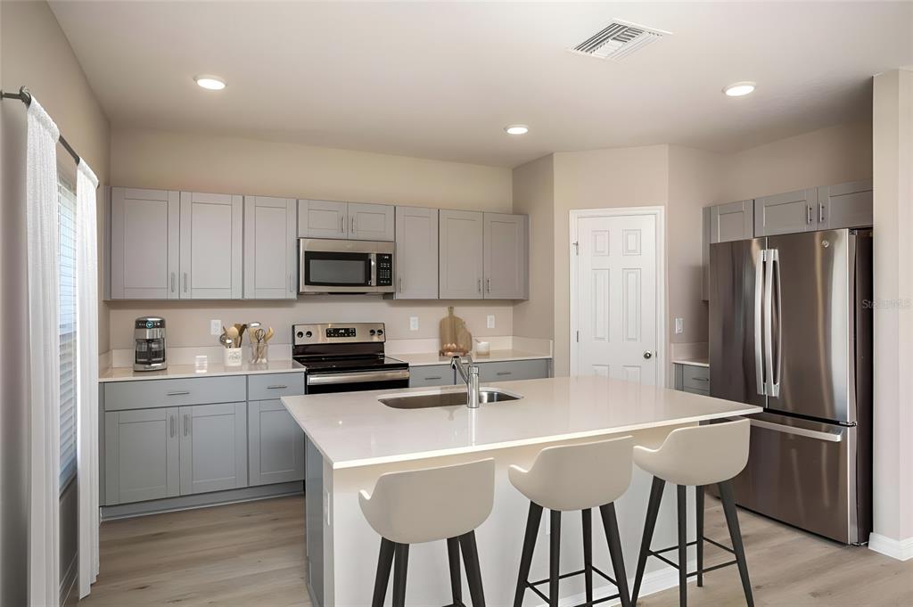A modern kitchen features gray cabinets, stainless steel appliances, a quartz island, and light flooring — 5836 HEAVEN ROAD, HAINES CITY, FL