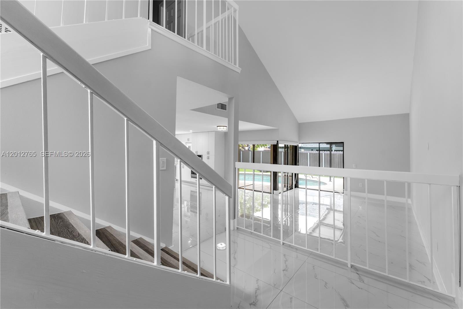 A staircase with dark wood treads and white railings overlooks a bright living area — 6327 SW 127th Pl, Miami FL 33183, MIAMI, FL