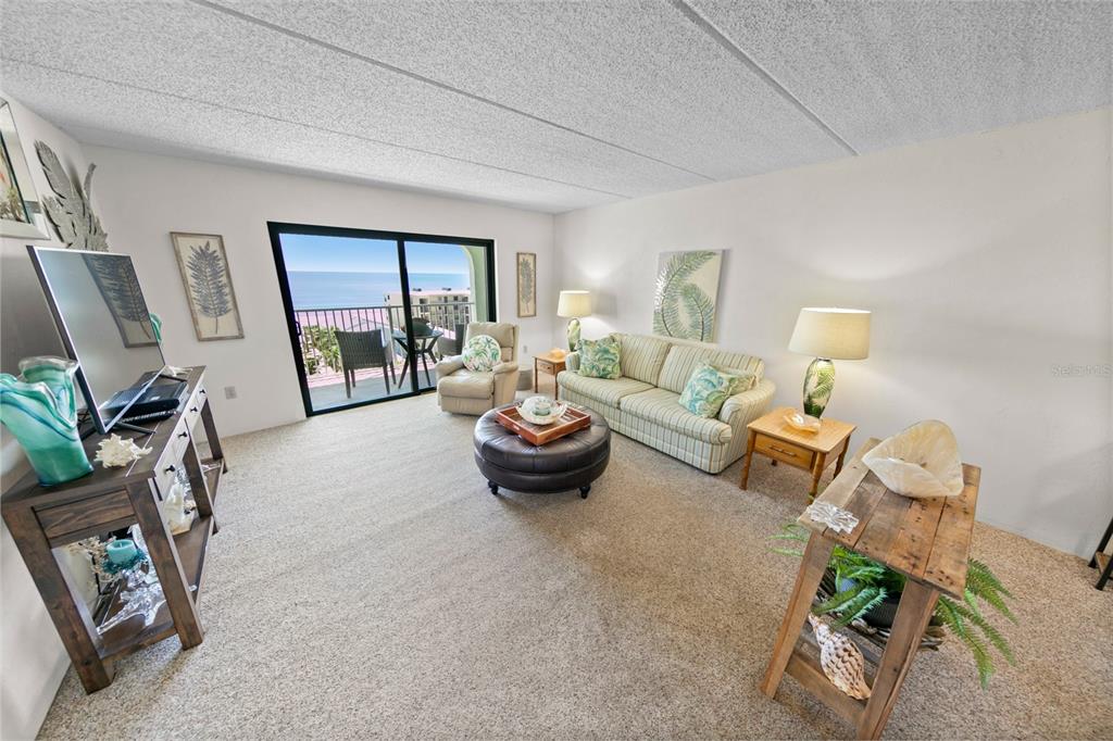 A living room features a striped sofa, a leather ottoman, and a balcony with ocean views — 3800 S ATLANTIC AVENUE UNIT 702, DAYTONA BEACH SHORES, FL