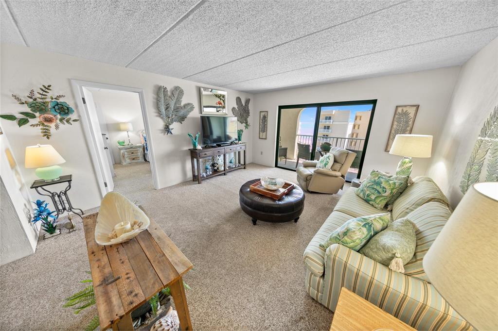 A living room features a striped sofa, leather ottoman, television console, and a balcony view — 3800 S ATLANTIC AVENUE UNIT 702, DAYTONA BEACH SHORES, FL
