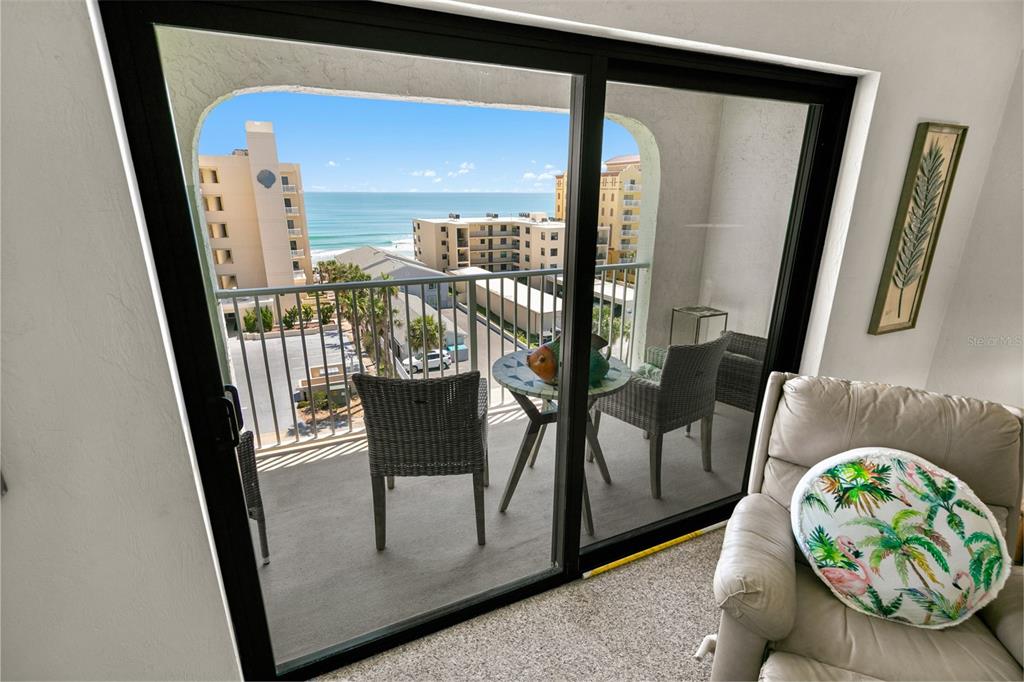 A view of a balcony with outdoor furniture overlooking the ocean through sliding glass doors — 3800 S ATLANTIC AVENUE UNIT 702, DAYTONA BEACH SHORES, FL