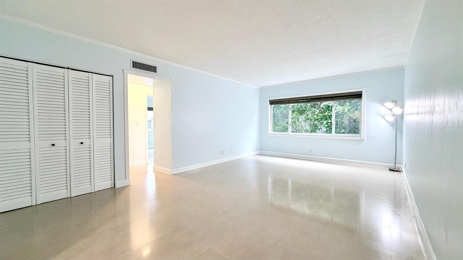 A bright, empty room features light blue walls, white louvered closet doors, and tile flooring — 251 SE 6th Avenue # 7, Pompano Beach FL 33060, POMPANO BEACH, FL