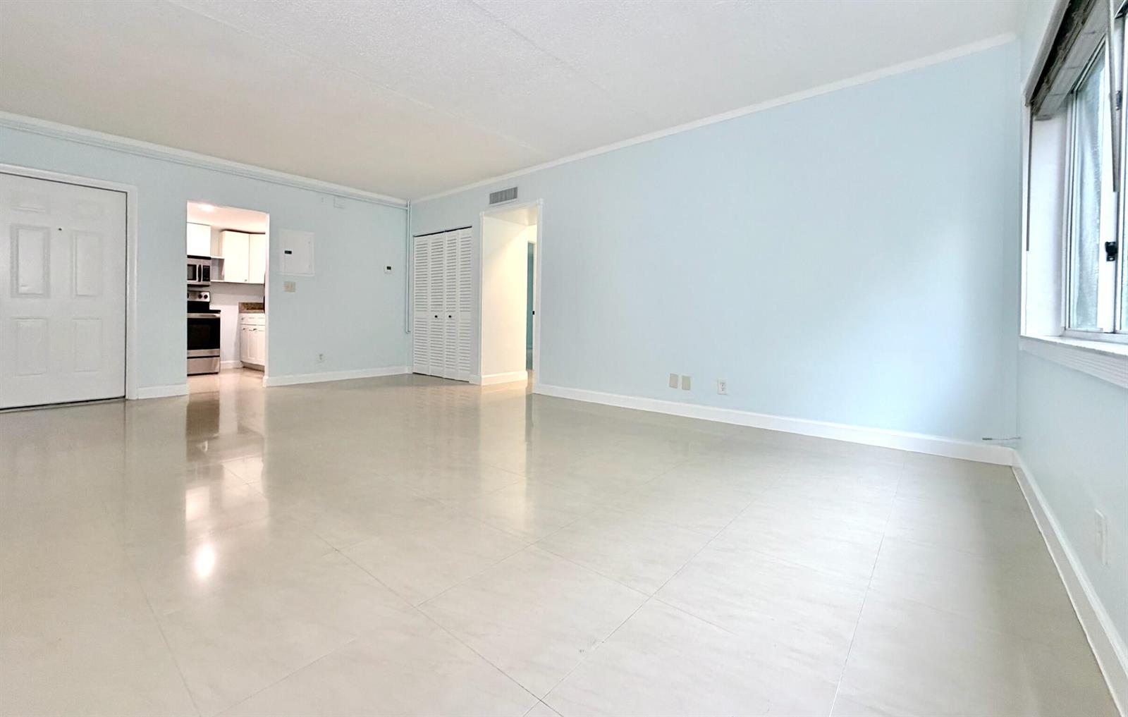 An empty living room features light blue walls, large beige floor tiles, and a window — 251 SE 6th Avenue # 7, Pompano Beach FL 33060, POMPANO BEACH, FL