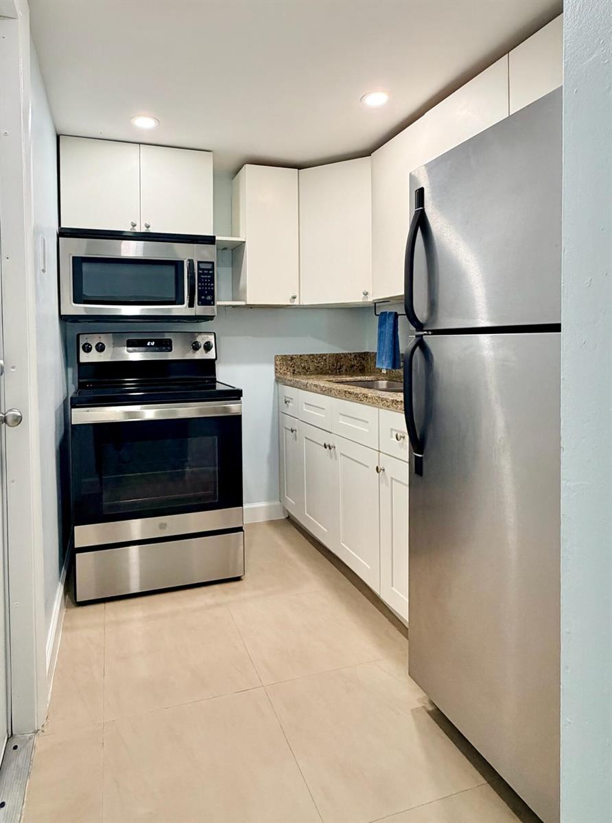 A galley kitchen features white cabinets, granite countertops, and stainless steel appliances — 251 SE 6th Avenue # 7, Pompano Beach FL 33060, POMPANO BEACH, FL