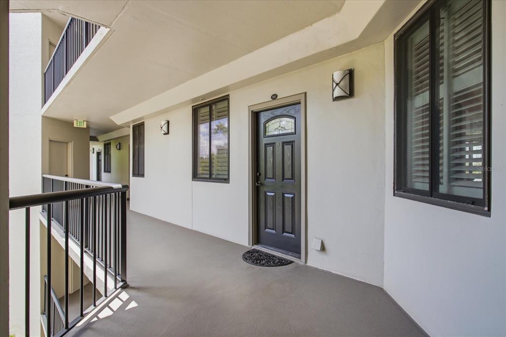 An exterior apartment hallway features a dark front door, a black metal railing, and windows — 401 E ROBINSON STREET UNIT 304, ORLANDO, FL