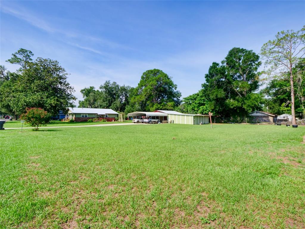 A large grassy yard leads to a house with a carport and detached storage building — 314 N YORK STREET, BUSHNELL, FL