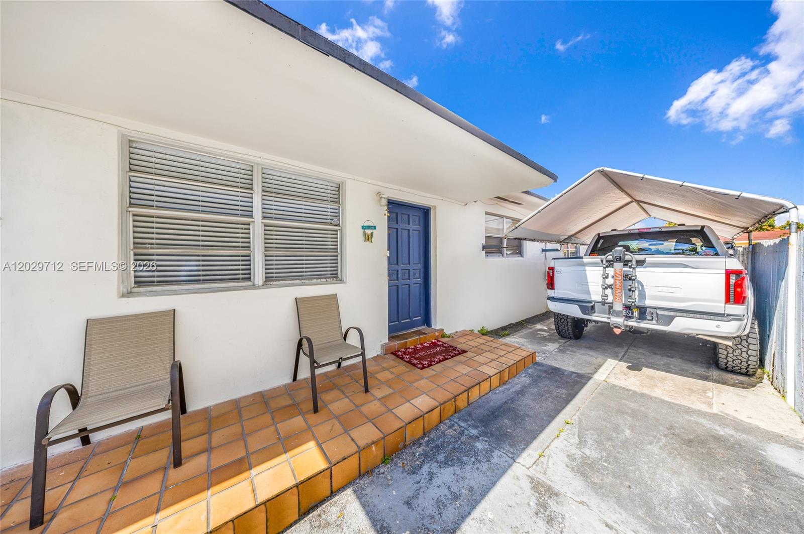 A white house exterior features a tiled porch, a blue door, and a covered parking area — 3532 NW 4th Ter, Miami FL 33125, MIAMI, FL
