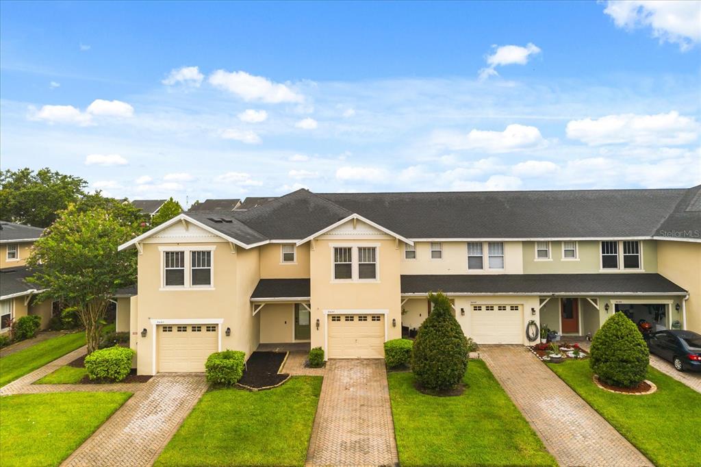An exterior view of a row of two-story townhouses with beige and green stucco facades — 5454 CARAMELLA DRIVE, ORLANDO, FL