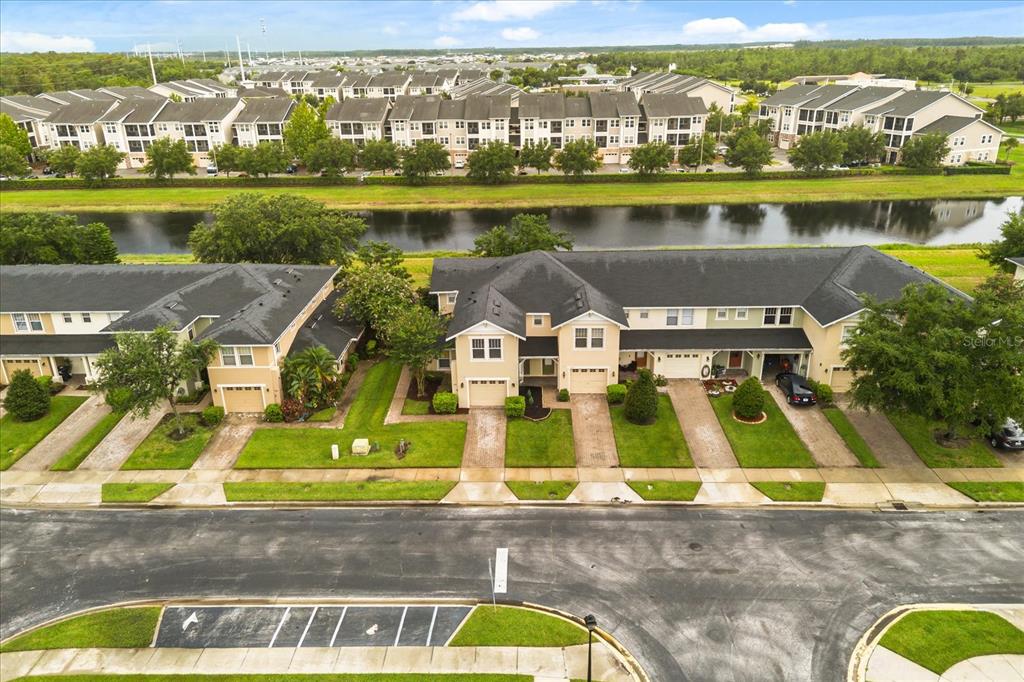 An aerial view shows a row of townhomes with attached garages facing a street and canal — 5454 CARAMELLA DRIVE, ORLANDO, FL