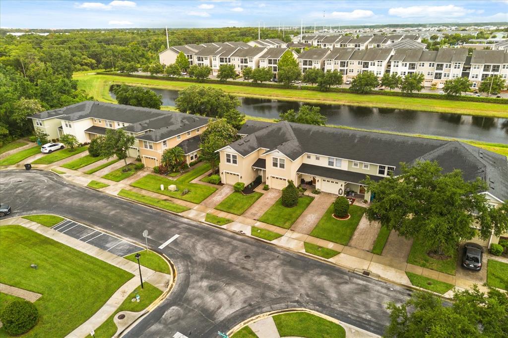 An aerial view shows two rows of townhouses with dark roofs near a small lake — 5454 CARAMELLA DRIVE, ORLANDO, FL