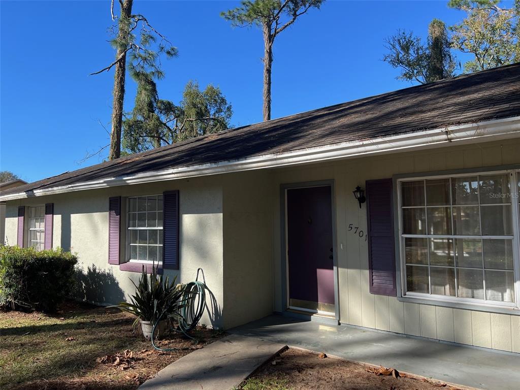 A single-story house exterior features light-colored siding, purple shutters, and a dark shingled roof — 5701 SE 2ND PLACE, OCALA, FL