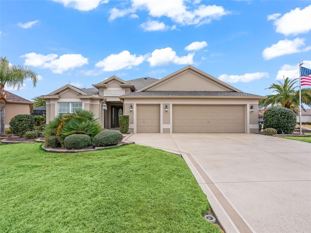 A single-story house with a beige exterior, a three-car garage, and a landscaped front yard — 3556 MISTLETOE COURT, THE VILLAGES, FL