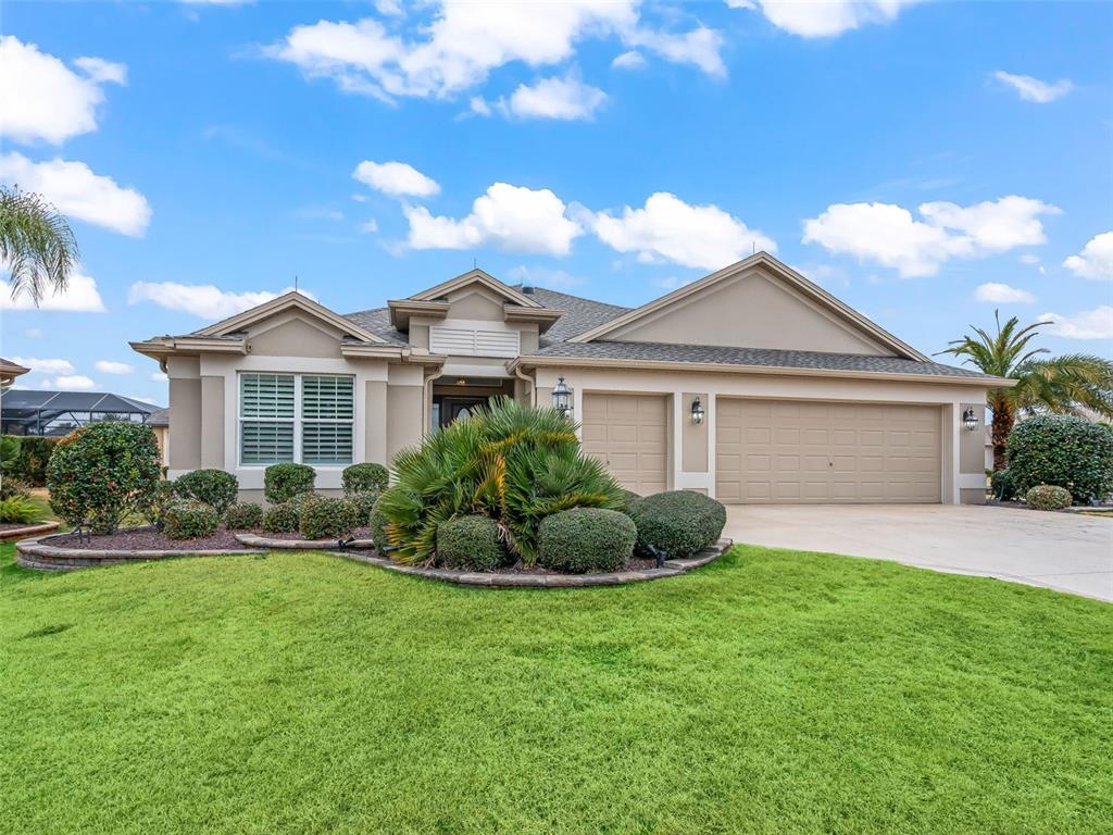 A single-story suburban house with a tan stucco exterior, a three-car garage, and landscaping — 3556 MISTLETOE COURT, THE VILLAGES, FL