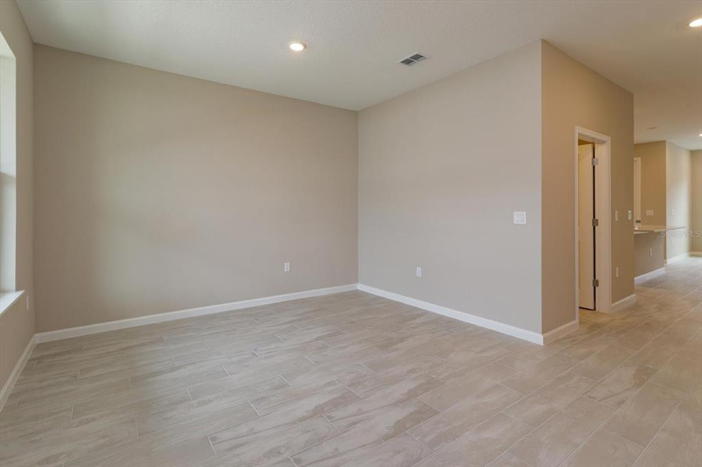 An empty room features light-colored wood-look tile flooring and beige walls — 13295 PEACEFUL MELODY DRIVE, WINTER GARDEN, FL