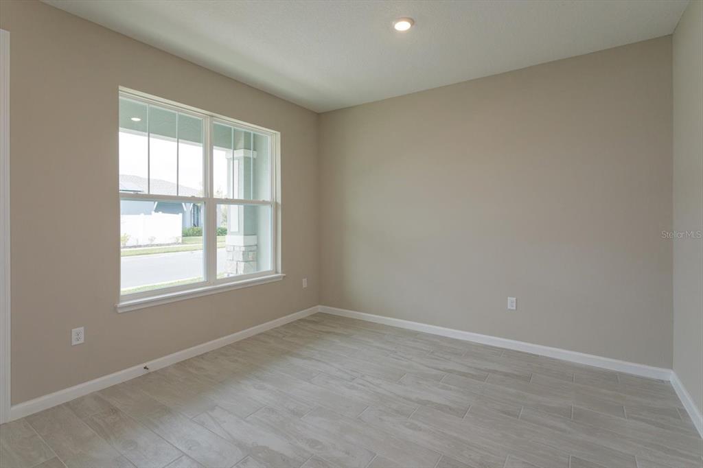 An empty room features light-colored tile flooring, beige walls, and a large window — 13295 PEACEFUL MELODY DRIVE, WINTER GARDEN, FL