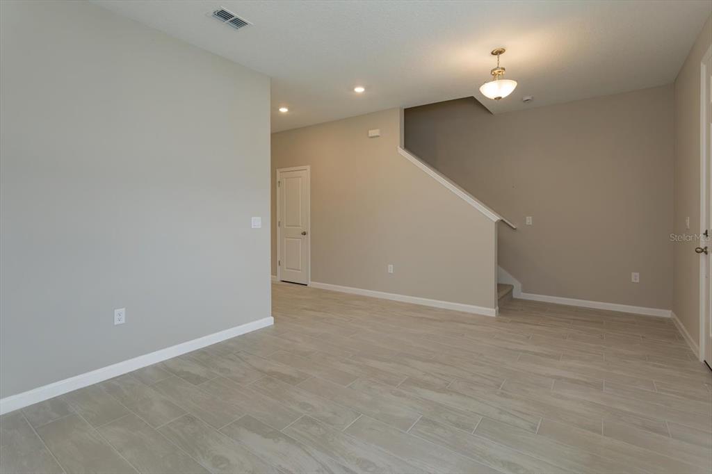 An interior view of a room with light-colored tile flooring, beige walls, and a staircase — 13295 PEACEFUL MELODY DRIVE, WINTER GARDEN, FL