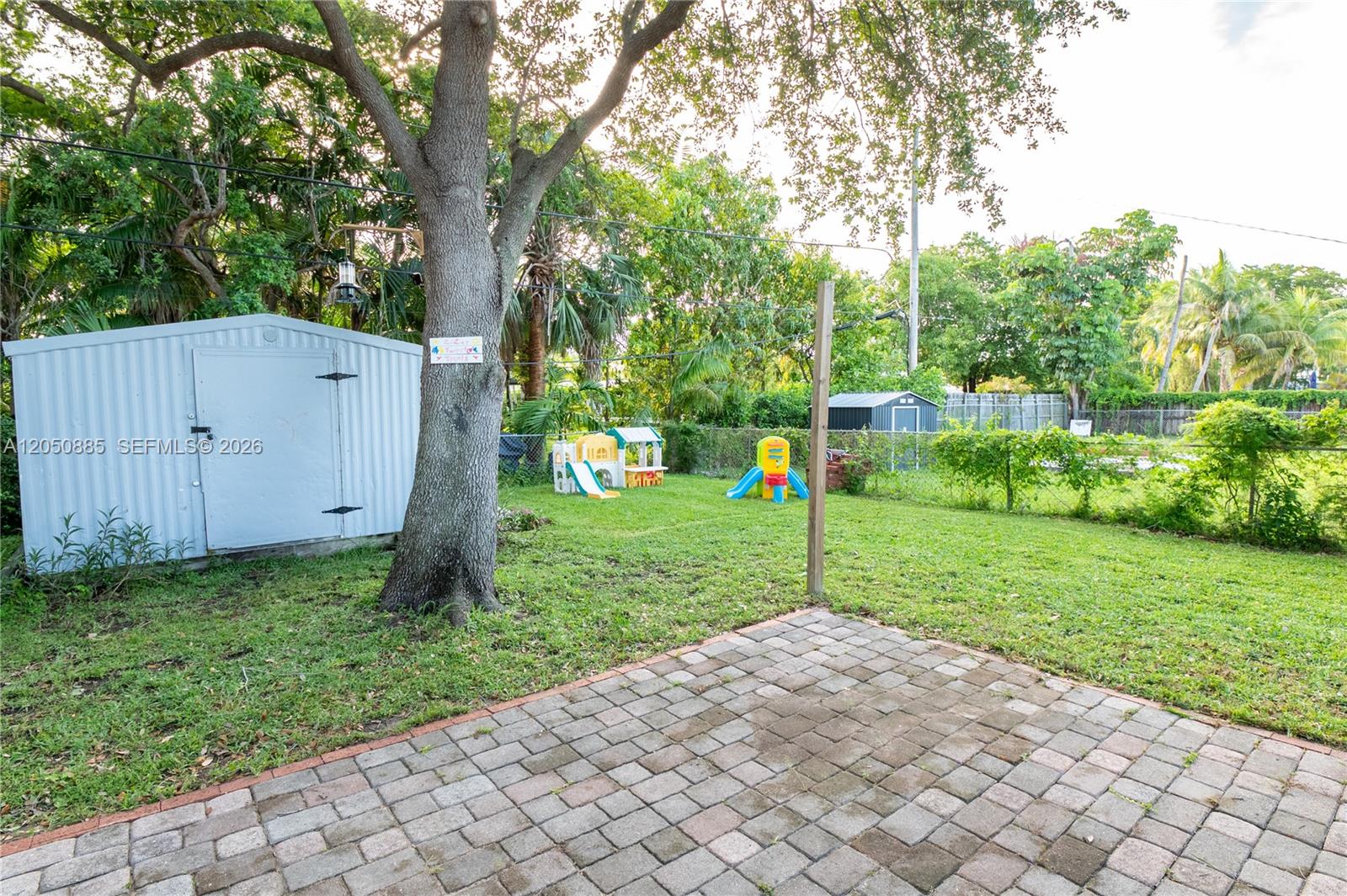A backyard features a paved patio, a storage shed, and children's play equipment under trees — 5030 SW 113th Ct, Miami FL 33165, MIAMI, FL