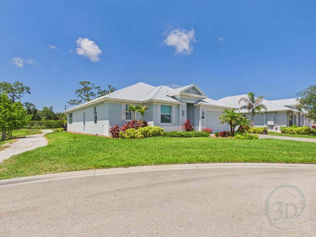 A light blue single-story house with a metal roof sits on a grassy corner lot — 5764 Arabella Lane, Vero Beach FL 32967, VERO BEACH, FL