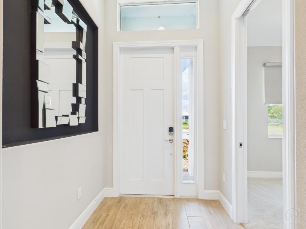 A bright entryway features a white front door, a side window, and a modern wall mirror — 5764 Arabella Lane, Vero Beach FL 32967, VERO BEACH, FL