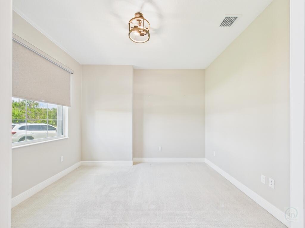 An empty room with beige carpet, light walls, a window with a shade, and a fixture — 5764 Arabella Lane, Vero Beach FL 32967, VERO BEACH, FL
