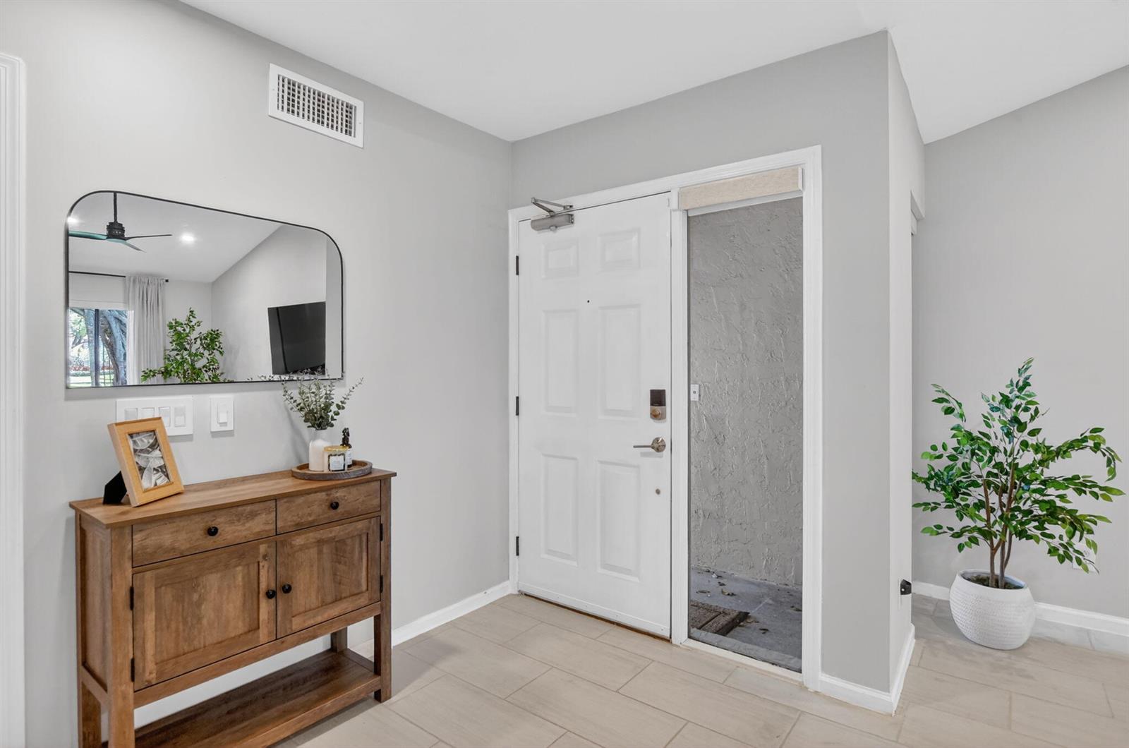 An entryway features a wooden console table, a wall mirror, and a white front door — 5530 Coach House Circle # A, Boca Raton FL 33486, BOCA RATON, FL