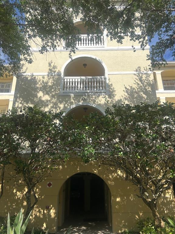 A multi-story tan stucco building features arched balconies with white railings and a ground-level entrance — 940 COOPER STREET UNIT 302, VENICE, FL