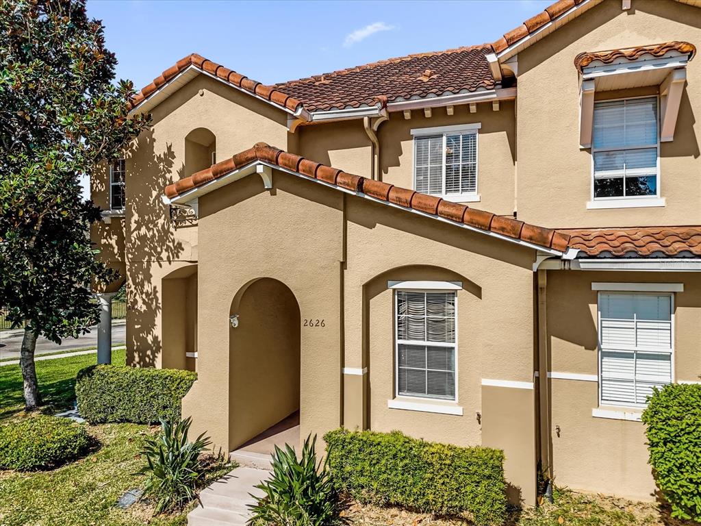 The exterior of a two-story tan stucco house features a tiled roof and arched entryway — 2626 ANDROS LANE, KISSIMMEE, FL