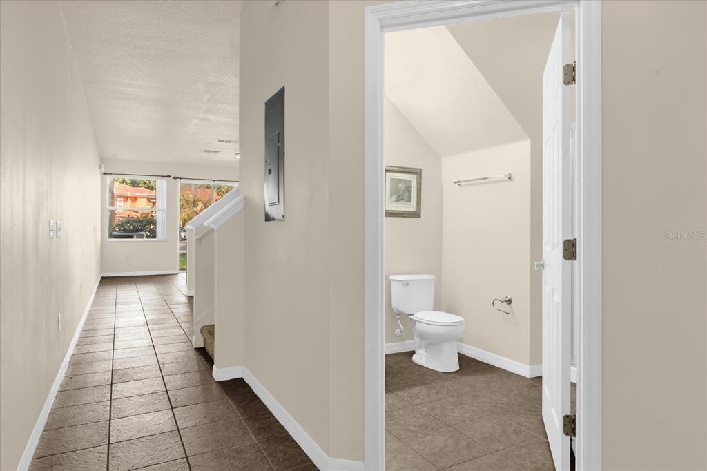 A hallway with tile flooring leads to a bathroom with a toilet and sloped ceiling — 2626 ANDROS LANE, KISSIMMEE, FL