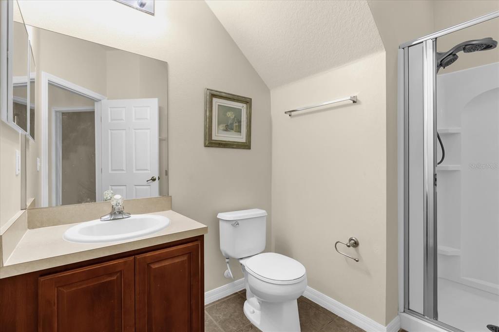 A bathroom with a wood vanity, white sink, toilet, and a glass-enclosed shower stall — 2626 ANDROS LANE, KISSIMMEE, FL