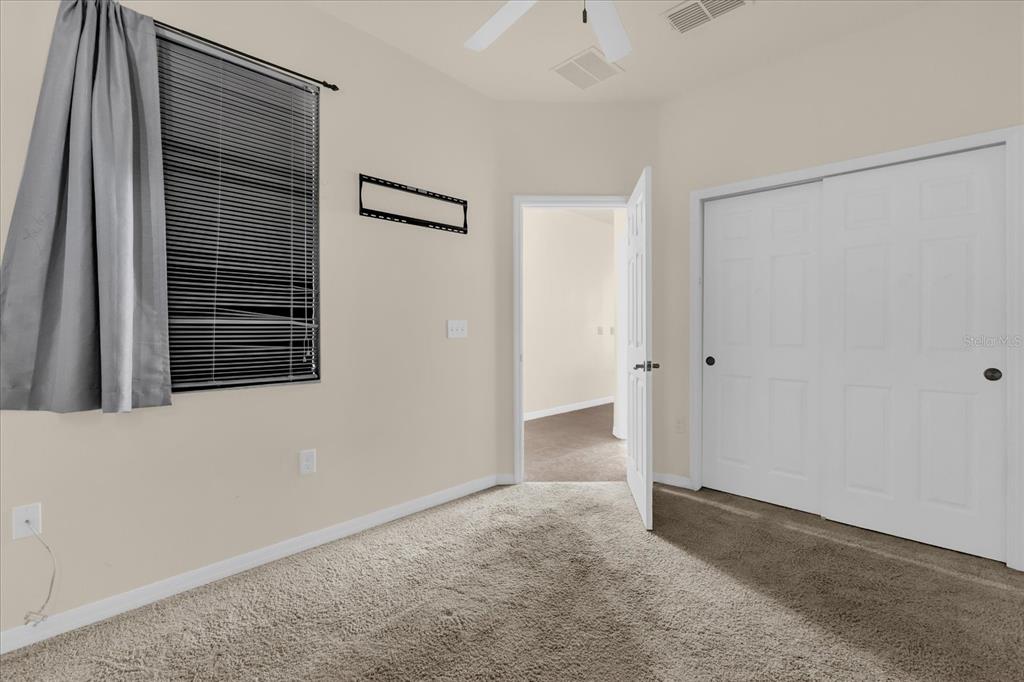 A bedroom features beige walls, carpeted flooring, a window with blinds, and white closet doors — 2626 ANDROS LANE, KISSIMMEE, FL
