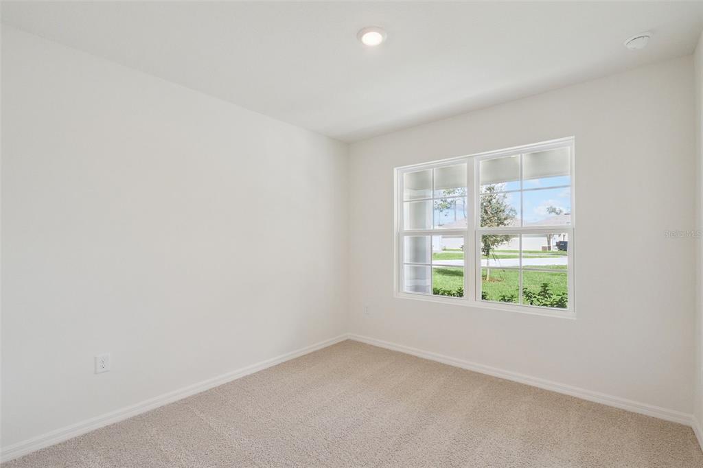 An empty bedroom features beige carpeting, white walls, and a window overlooking a grassy yard — 1168 MORFONTAINE STREET, DAYTONA BEACH, FL