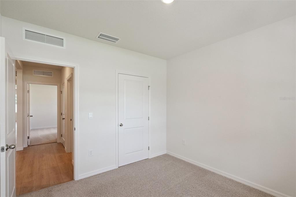 An empty bedroom features beige carpet, white walls, and a closed white door — 1168 MORFONTAINE STREET, DAYTONA BEACH, FL