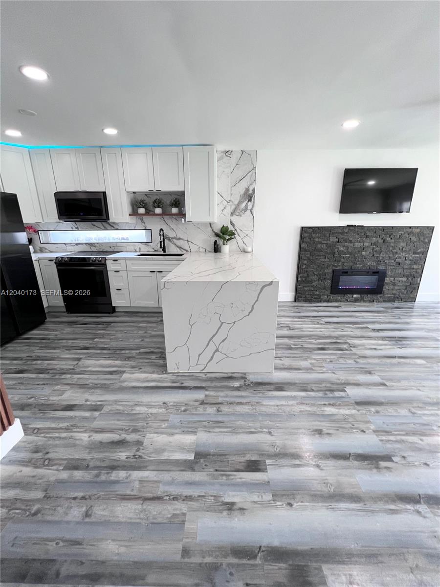 A modern kitchen features white cabinets, a waterfall quartz island, and an adjacent stone fireplace — 2425 SW 26th Ln, Miami FL 33133, MIAMI, FL
