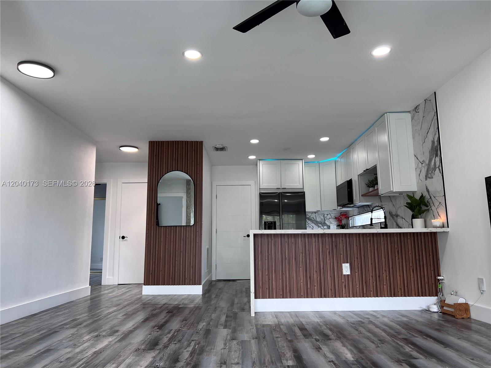 A kitchen features wood-slat paneling, white cabinets, marble-patterned backsplashes, and grey wood-look flooring — 2425 SW 26th Ln, Miami FL 33133, MIAMI, FL