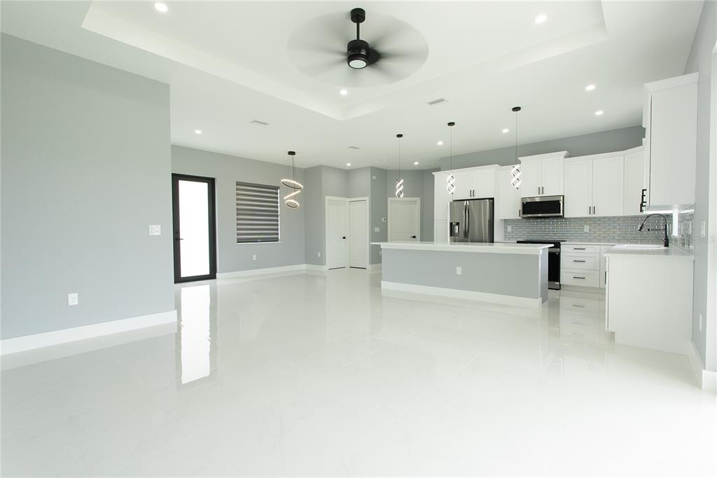 A modern open-concept kitchen and living area with white cabinetry, tile floors, and recessed lighting — 3508 29TH STREET SW, LEHIGH ACRES, FL