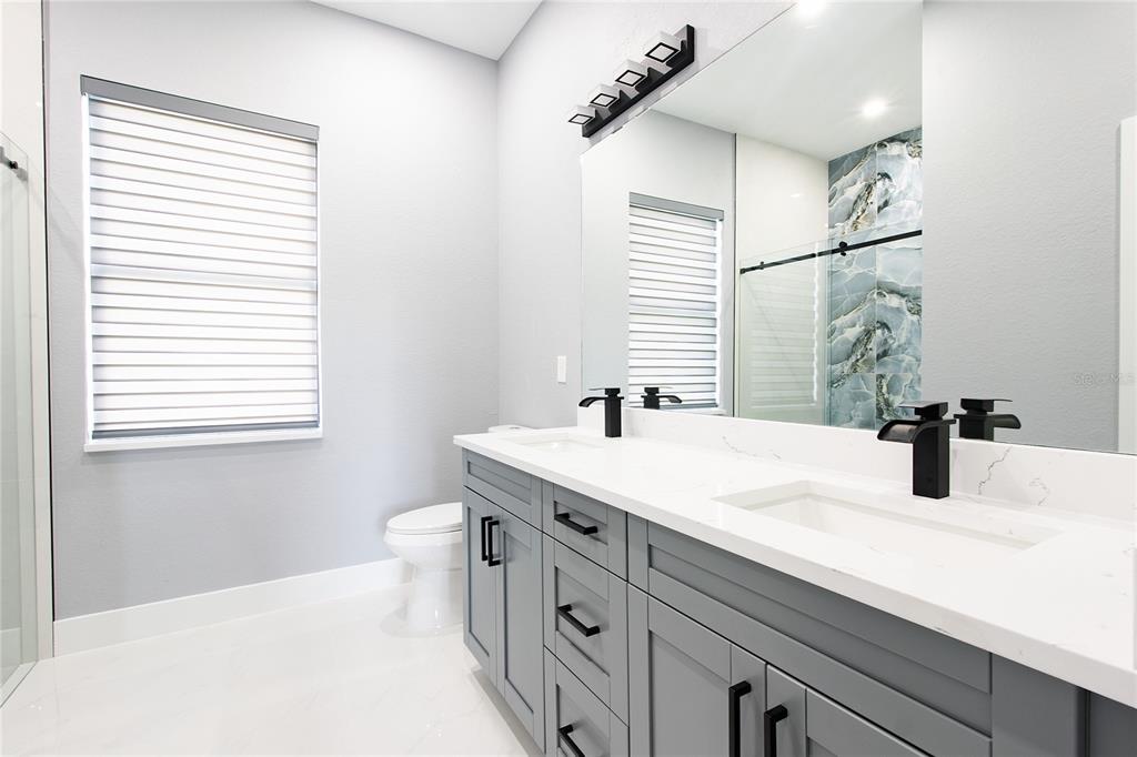 A modern bathroom features a double vanity with gray cabinets, white countertops, and black fixtures — 3508 29TH STREET SW, LEHIGH ACRES, FL