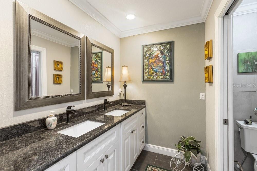 A bathroom with a double vanity, dark granite countertops, white cabinets, and two framed mirrors — 13502 WHITBY ROAD, HUDSON, FL
