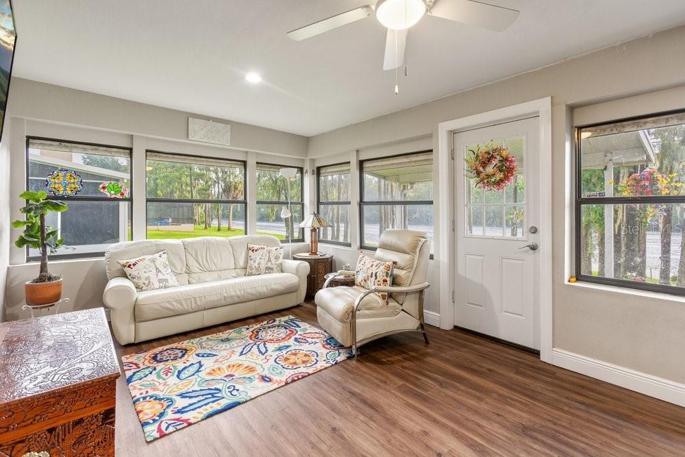 A sunroom with wood-look flooring, a white sofa, a recliner, and large windows — 13502 WHITBY ROAD, HUDSON, FL