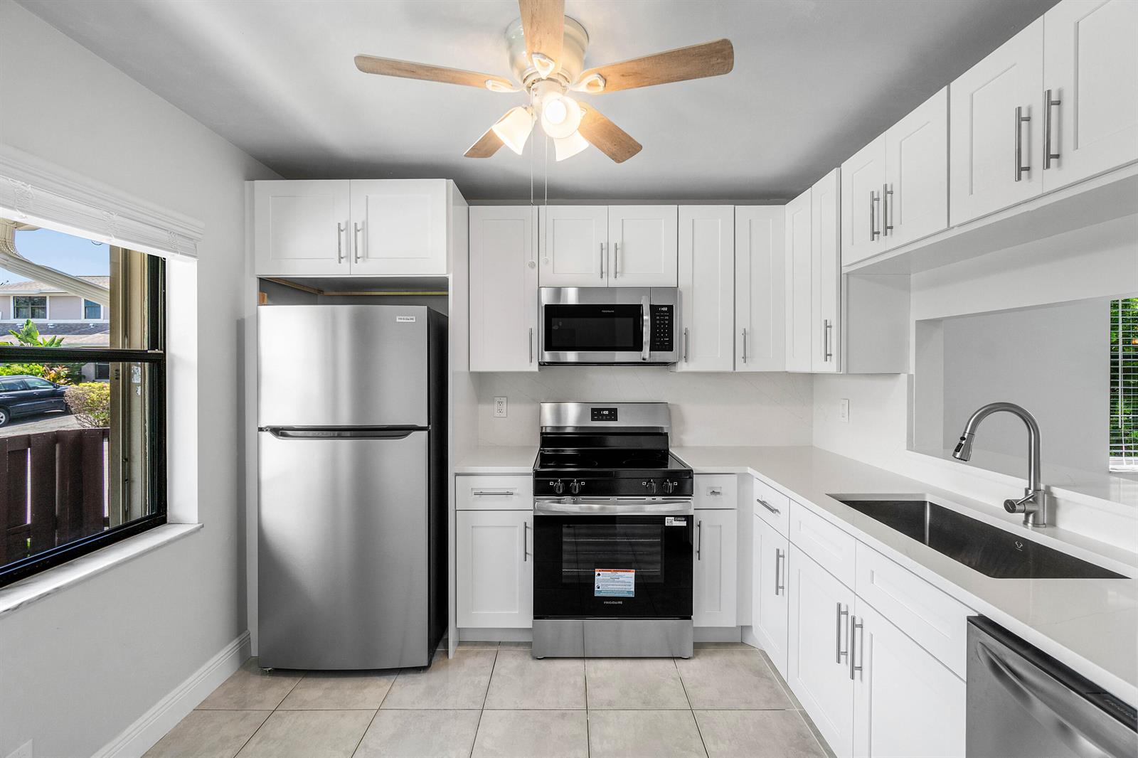 A kitchen features white cabinets, stainless steel appliances, a ceiling fan, and a window view — 5162 Tennis Lane, Delray Beach FL 33484, DELRAY BEACH, FL