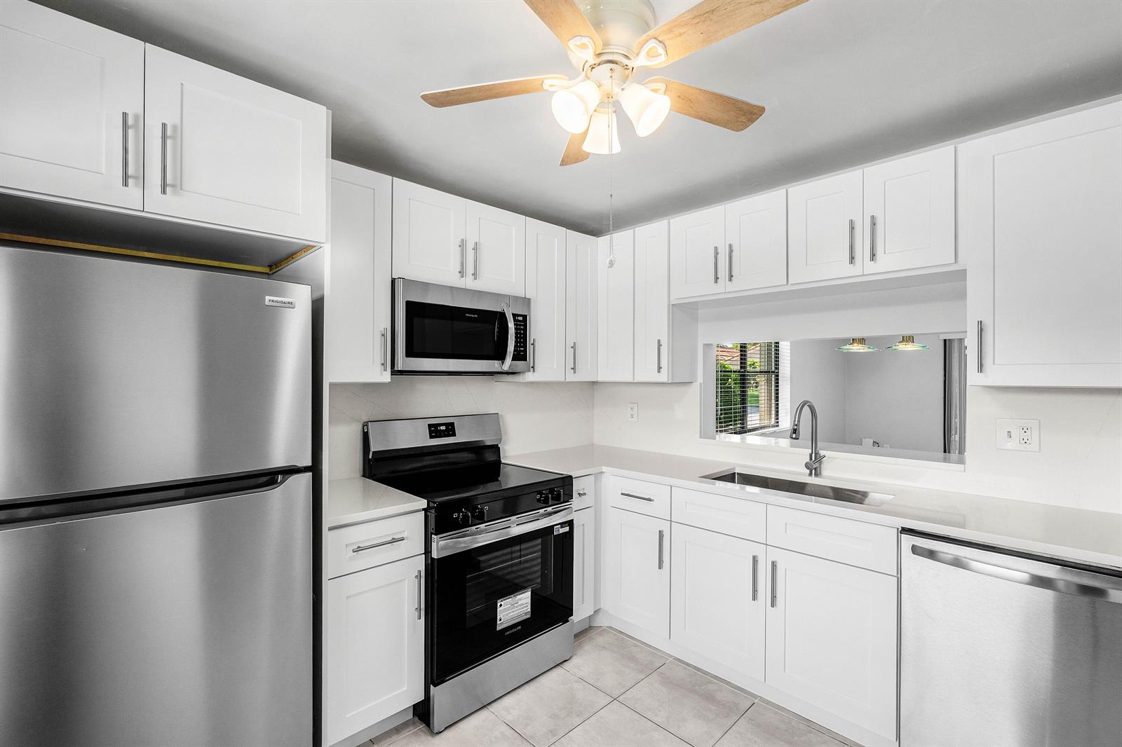 A kitchen with white cabinets, stainless steel appliances, and a pass-through window above the sink — 5162 Tennis Lane, Delray Beach FL 33484, DELRAY BEACH, FL