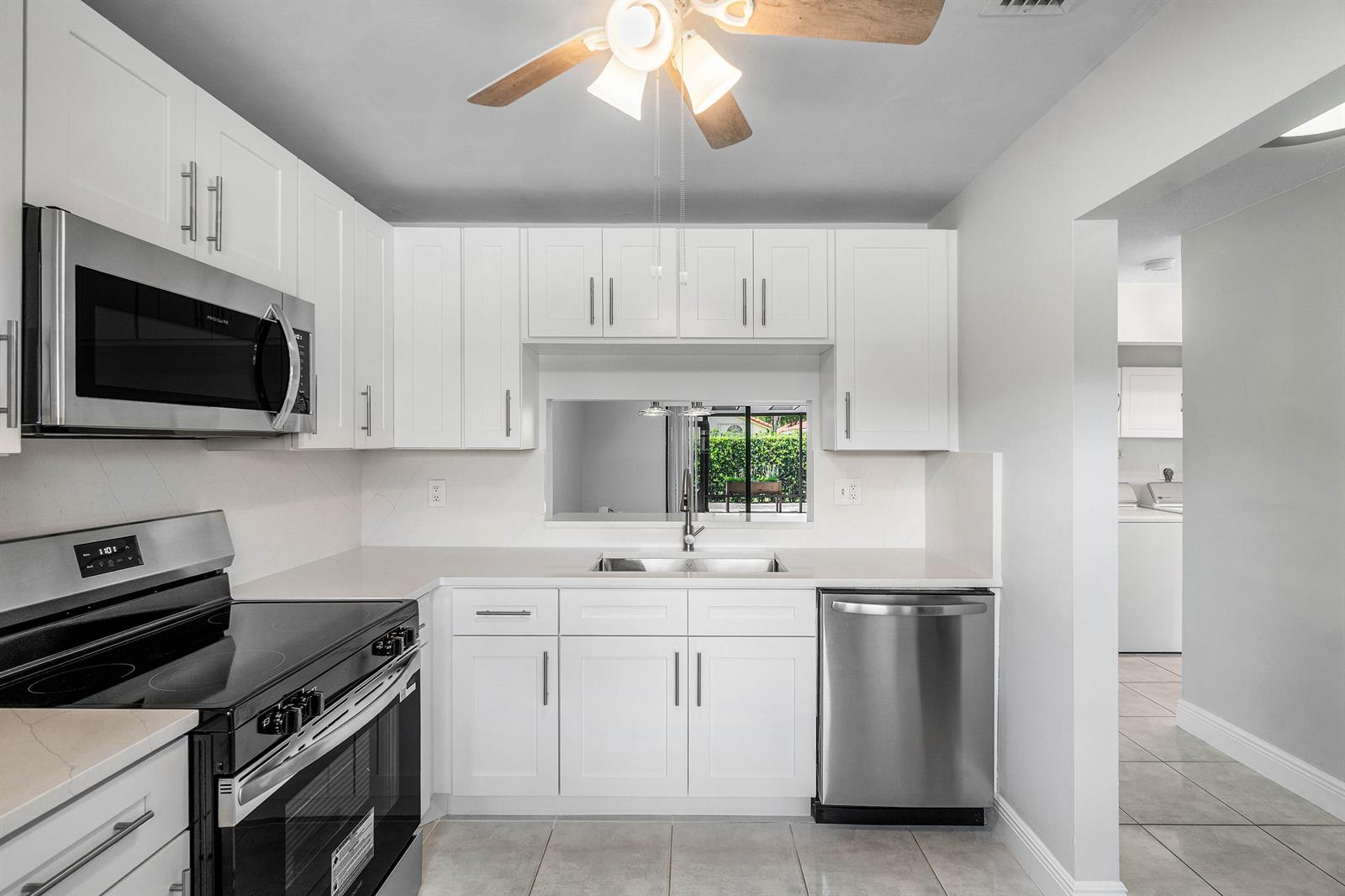 A kitchen with white cabinets, stainless steel appliances, and a pass-through window to the outdoors — 5162 Tennis Lane, Delray Beach FL 33484, DELRAY BEACH, FL