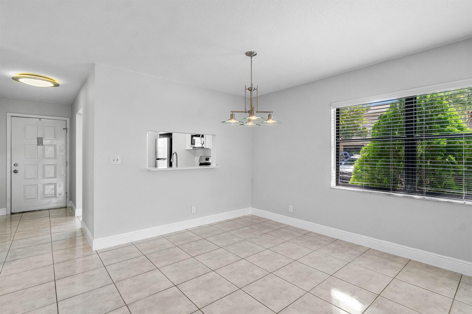A dining area with light tile flooring, a chandelier, and a pass-through window to the kitchen — 5162 Tennis Lane, Delray Beach FL 33484, DELRAY BEACH, FL